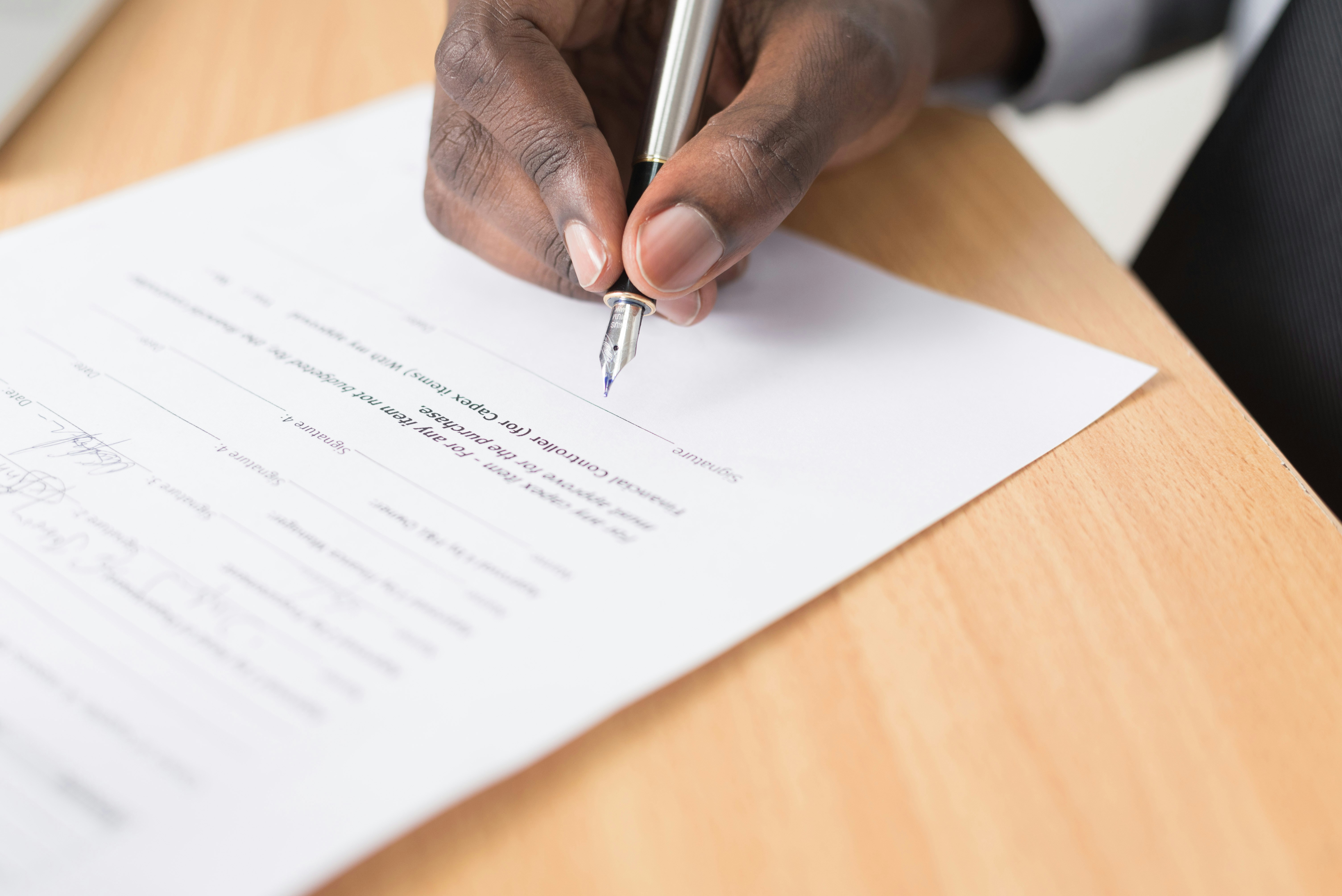 Close-up of a person signing a form with a pen on a wooden desk