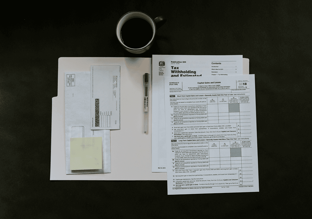 Overhead view of tax documents, envelopes, a pen, and a coffee cup arranged on a dark desk.