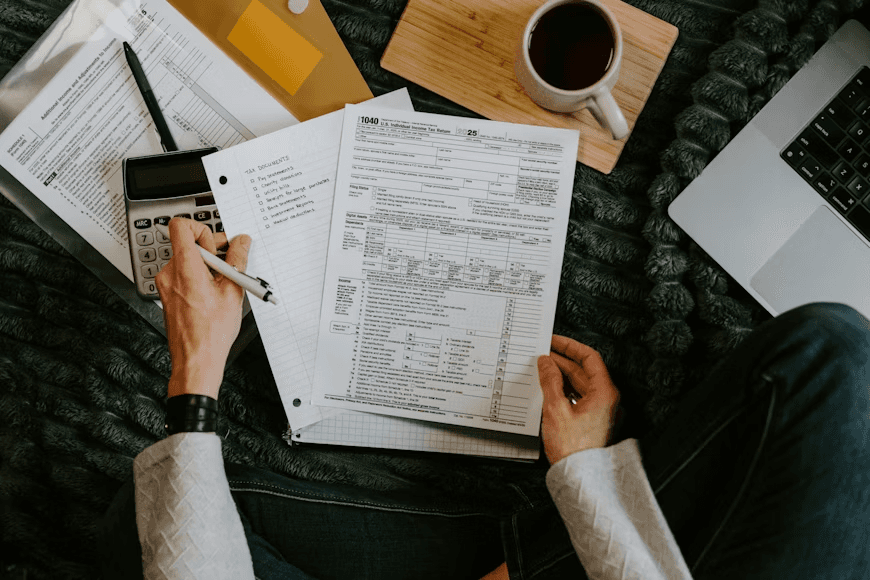 Person reviewing tax documents with a calculator and laptop before meeting a tax lawyer.