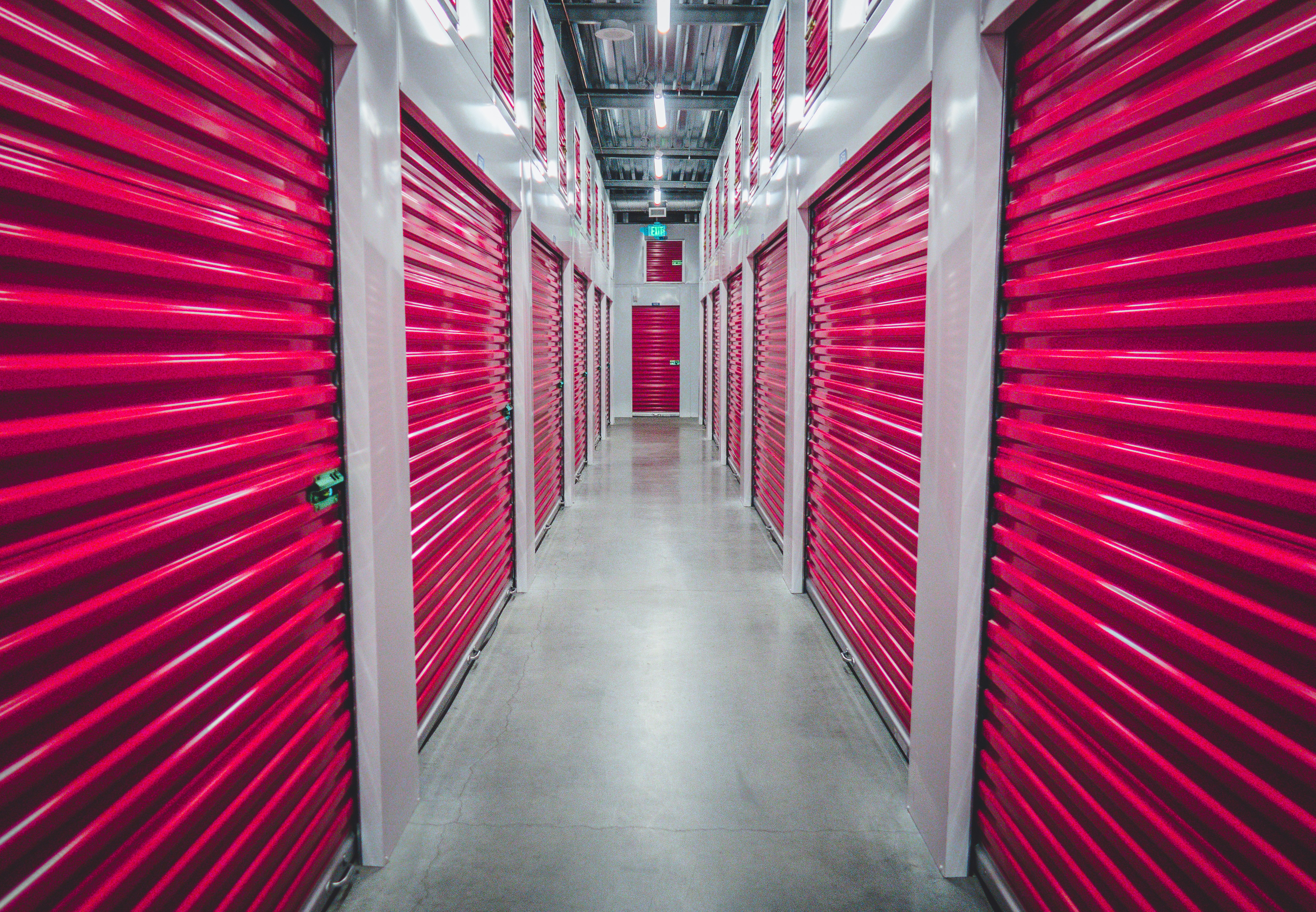 Indoor storage unit corridor with bright lighting and multiple red metal storage doors.