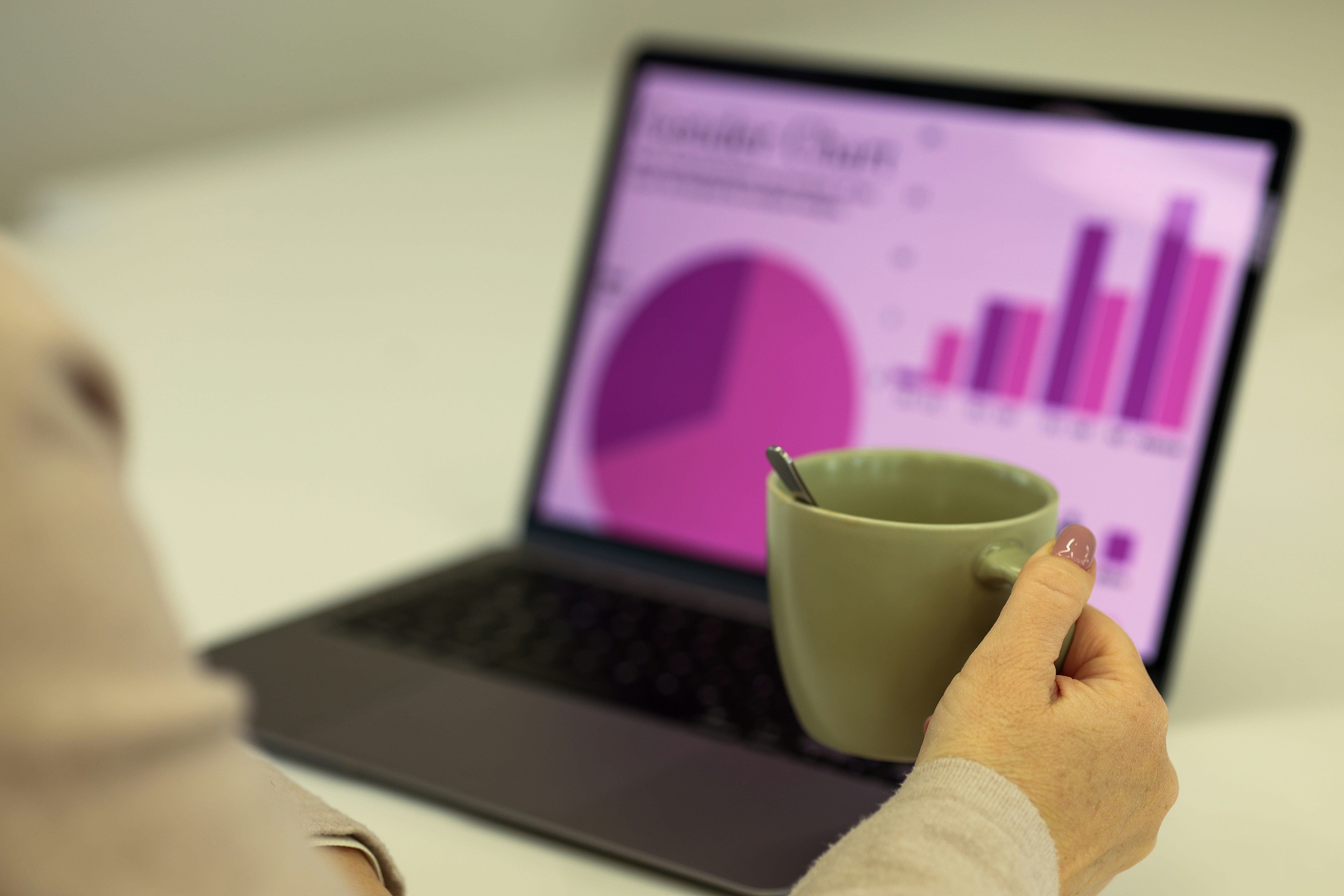 Person holding a coffee mug while viewing charts and graphs on a laptop screen
