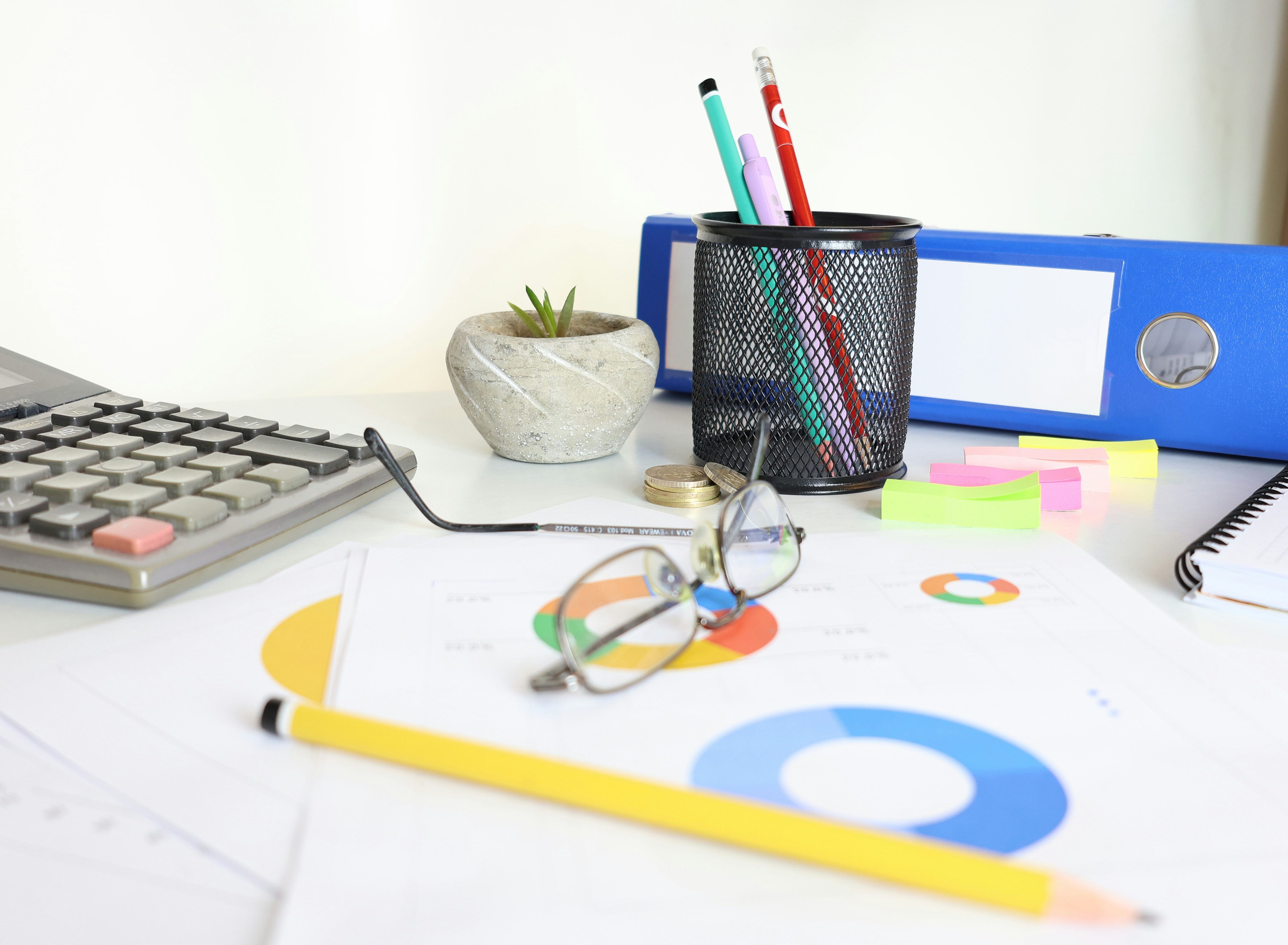 Office desk with calculator, charts, eyeglasses, pens, sticky notes, and a blue binder arranged for financial planning.