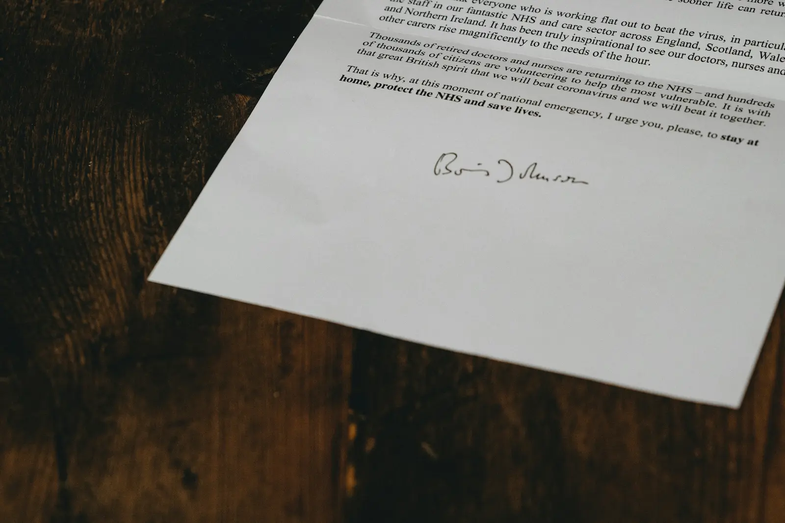 A close-up of a printed document on a wooden table, focusing on the handwritten signature at the bottom.