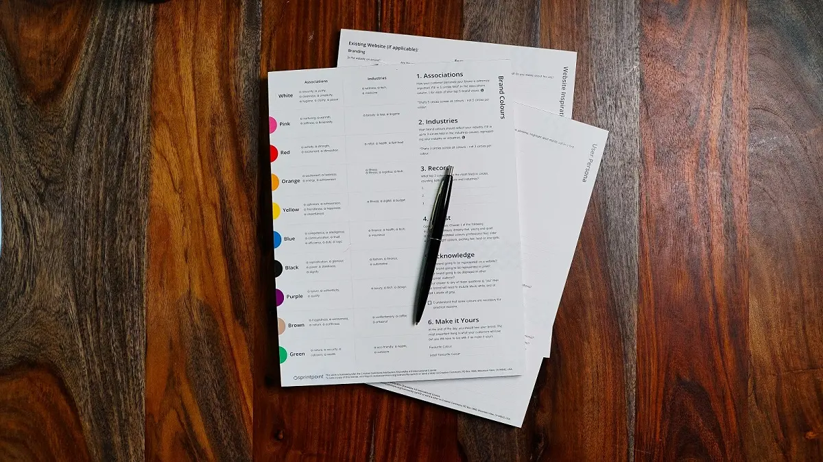 Stack of printed documents with a pen on a wooden table, viewed from above.