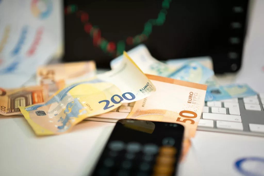 Euro banknotes on a desk with a calculator and financial chart.