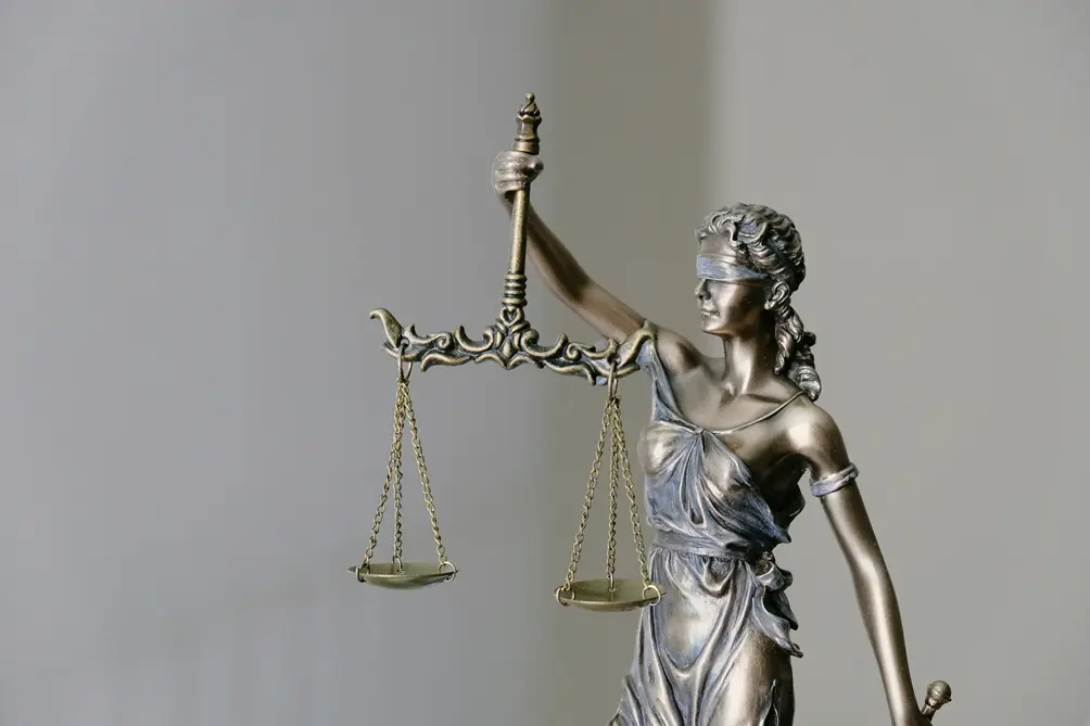 A metallic justice figure with one arm raised, suspending two scales on chains
