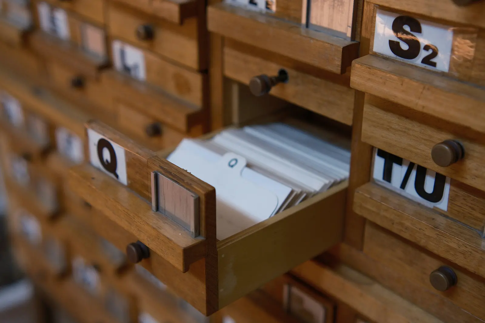 A close-up of a wooden card-catalog cabinet with one drawer pulled open, showing neatly stacked index cards inside.