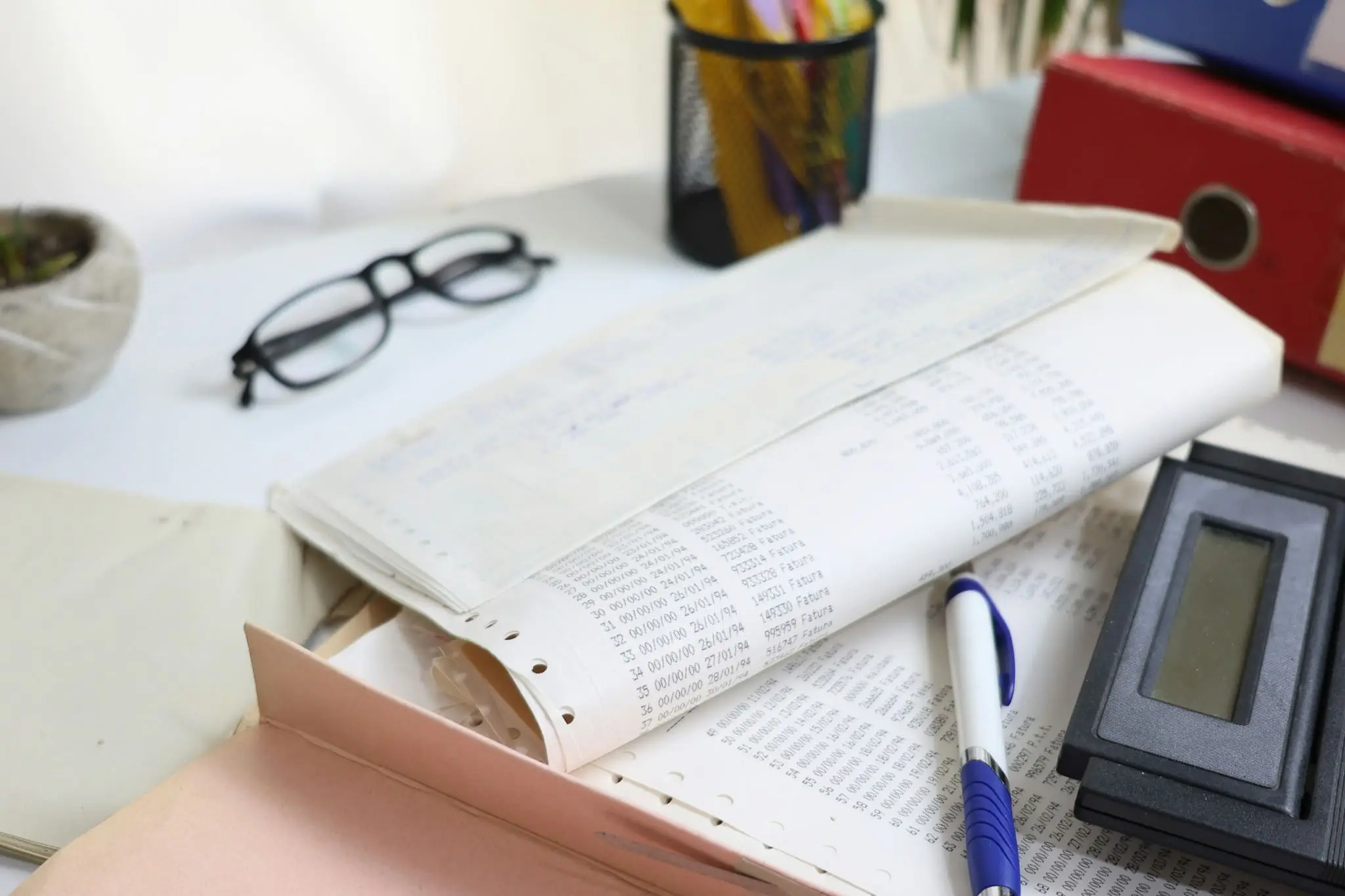 Stack of paperwork with a calculator, pen, and glasses on a desk.