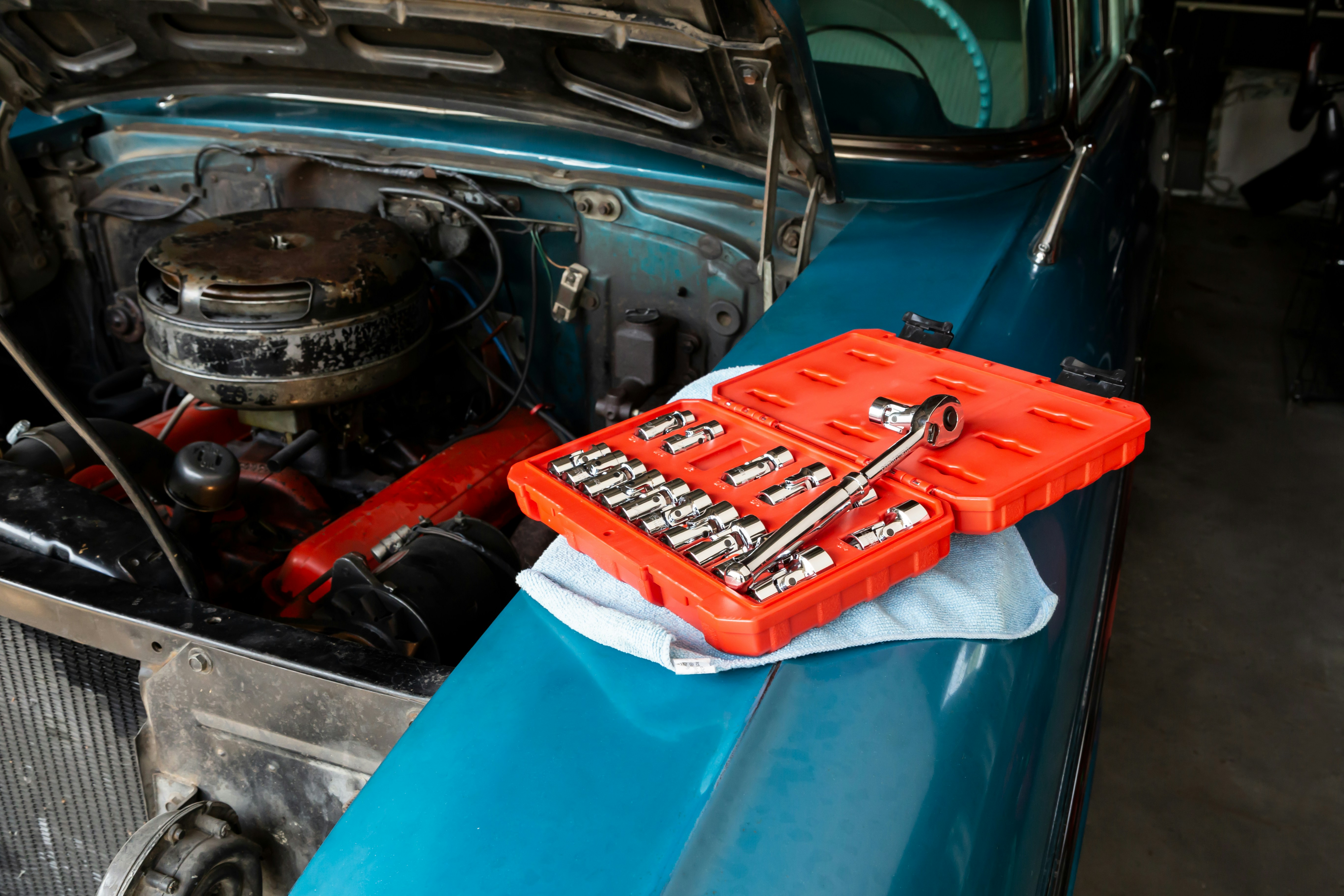 Open socket wrench set on the fender of a classic car with the hood raised.